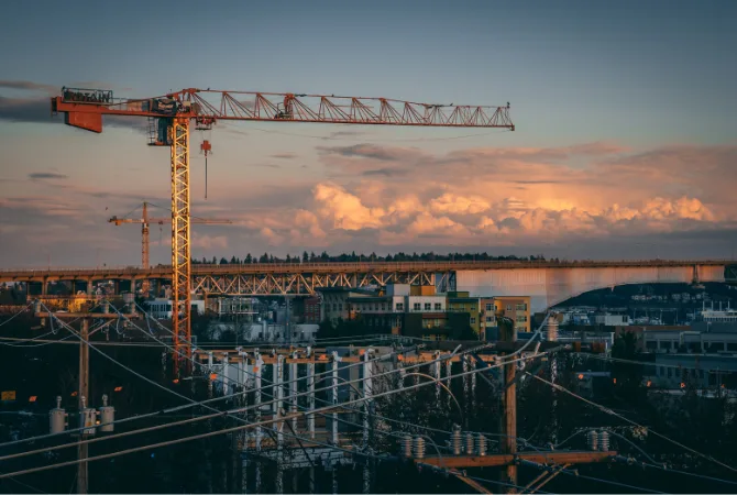 Urban construction site at sunset featuring a tower crane, industrial buildings, and city infrastructure under development