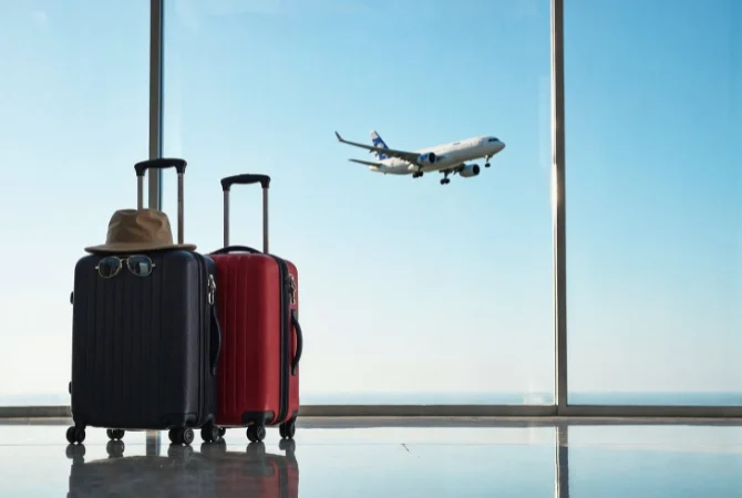 Travel luggage at airport terminal with airplane taking off in the background, representing vacation and air travel.