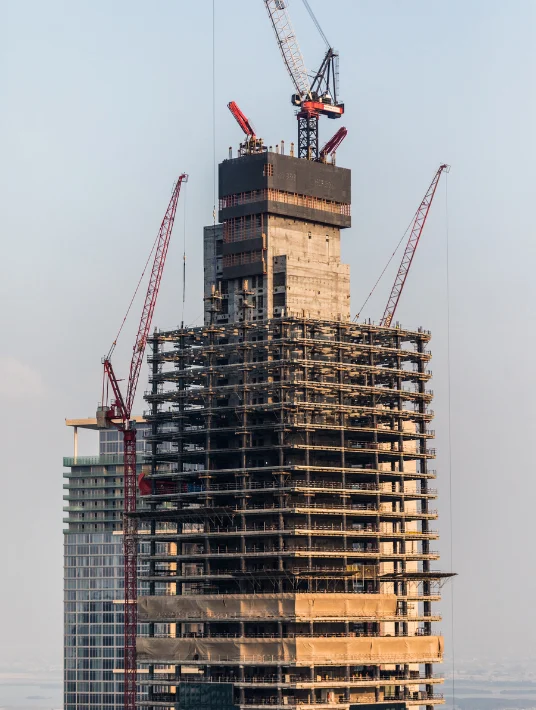 Close-up of a skyscraper under construction with cranes at work, showing the top section of the building and scaffolding