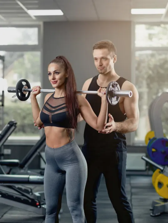 Three people relaxing in a gym after a workout. Two women and one man are sitting on the floor in fitness attire, surrounded by gym equipment such as kettlebells, dumbbells, and water bottles