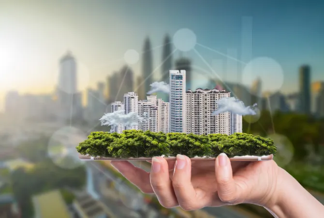 A hand holding a smartphone displaying a miniature model of a city with skyscrapers and trees, symbolizing urban development and technology