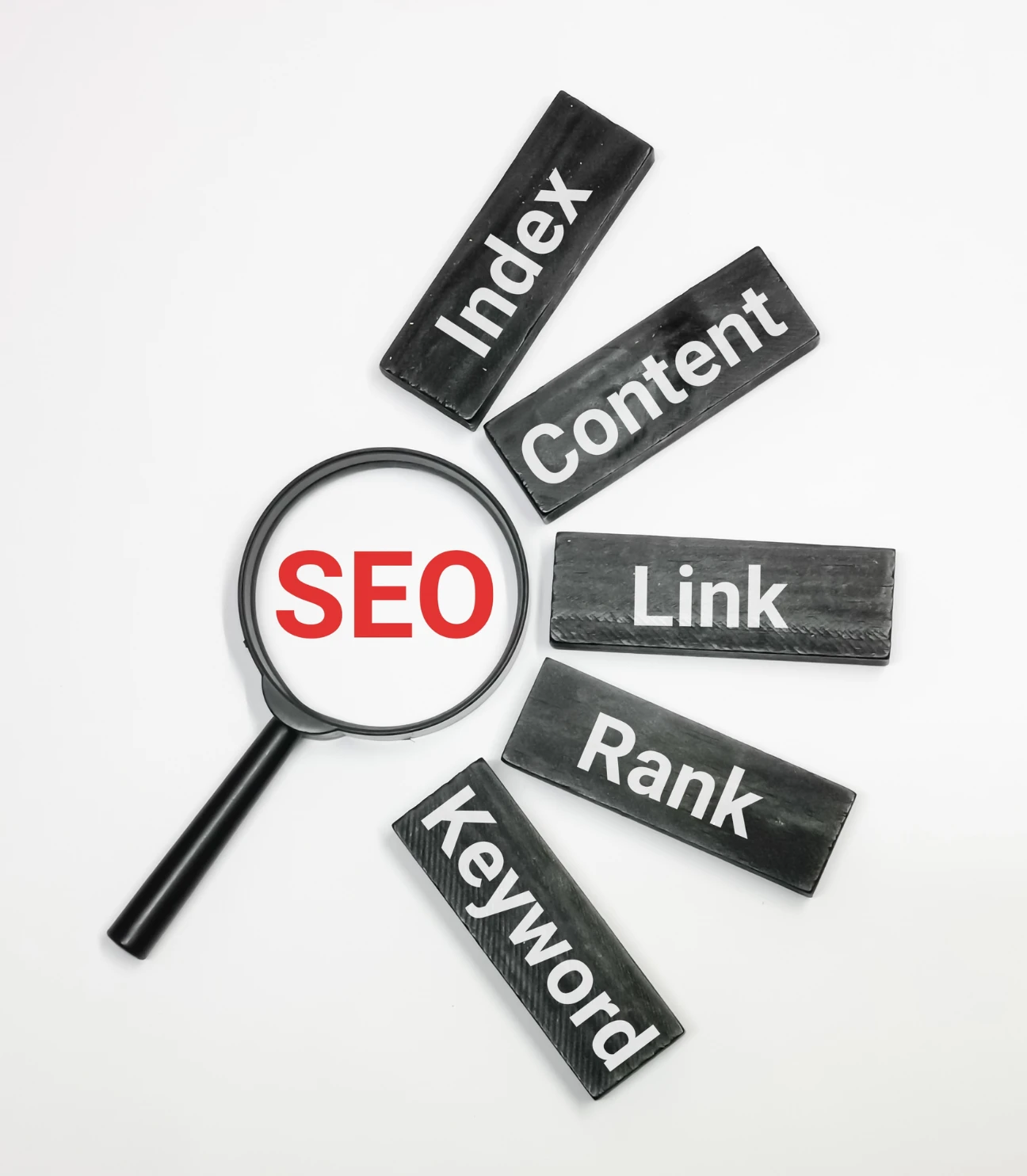 A magnifying glass focusing on the word 'SEO,' with surrounding blocks labeled 'Index,' 'Content,' 'Link,' 'Rank,' and 'Keyword.' The image visually represents key elements of Search Engine Optimization (SEO).