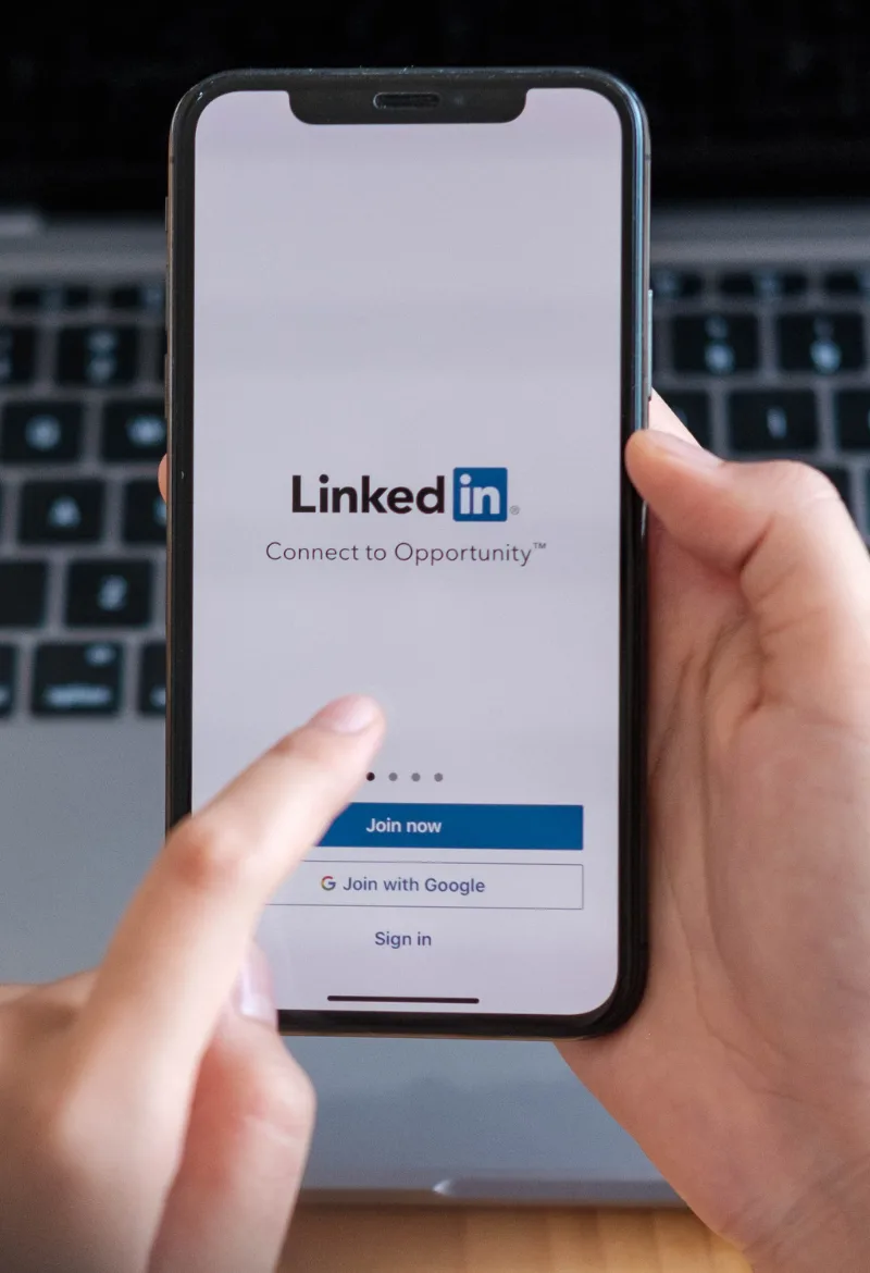 A person holding a smartphone with the LinkedIn login screen visible.
