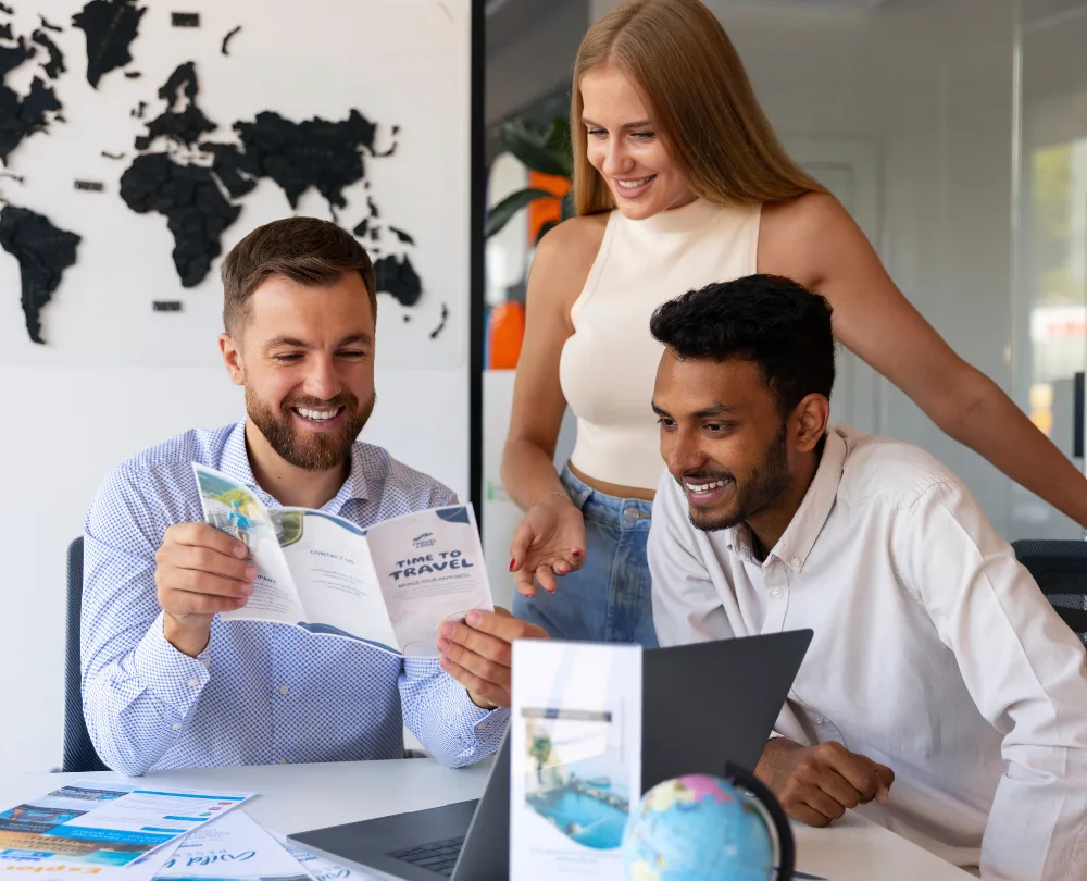 Three people in an office, reviewing a travel brochure and laptop, with a world map in the background.