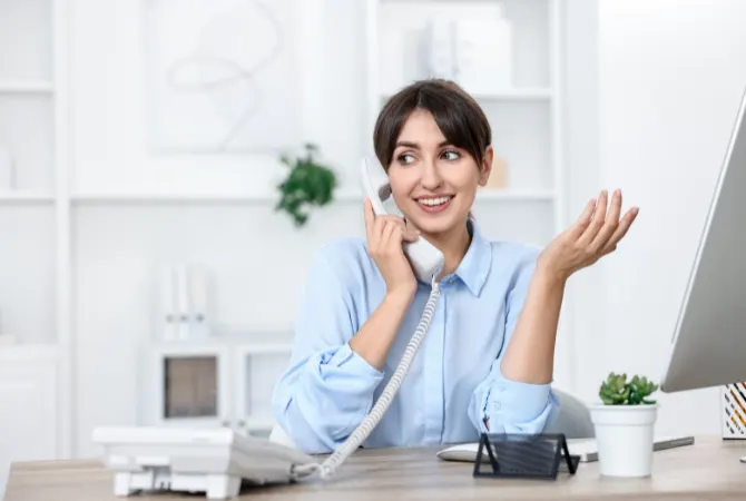 Smiling woman talking on the phone in an office, gesturing with her hand, representing a friendly consultation experience for potential clients